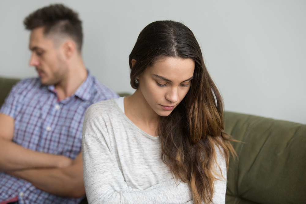 Concerned serious wife sad about family problem, thinking about relationships ending, husband sitting behind being ignorant and indifferent. Concept of spouse break up, unsuccessful marriage, quarrel